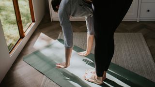 Woman rolling down to touch toes while standing on a yoga mat at home studio