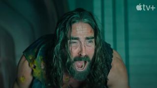 a long-haired, bearded man in rags screams in agony inside a stone corridor