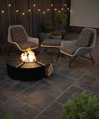 paved patio with a lit fire pit and festoon lights hanging on a fence