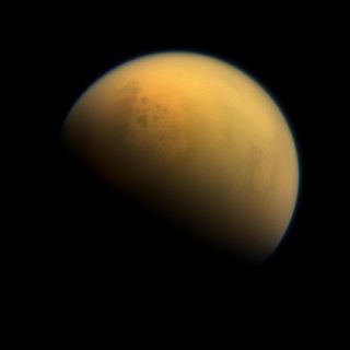 Saturn's largest moon Titan has a thick, smoggy atmosphere and is home to vast lakes of liquid methane, which are visible in this image as darker blotches in the moon's upper right. Titan's largest sea is called the Kraken Mare.