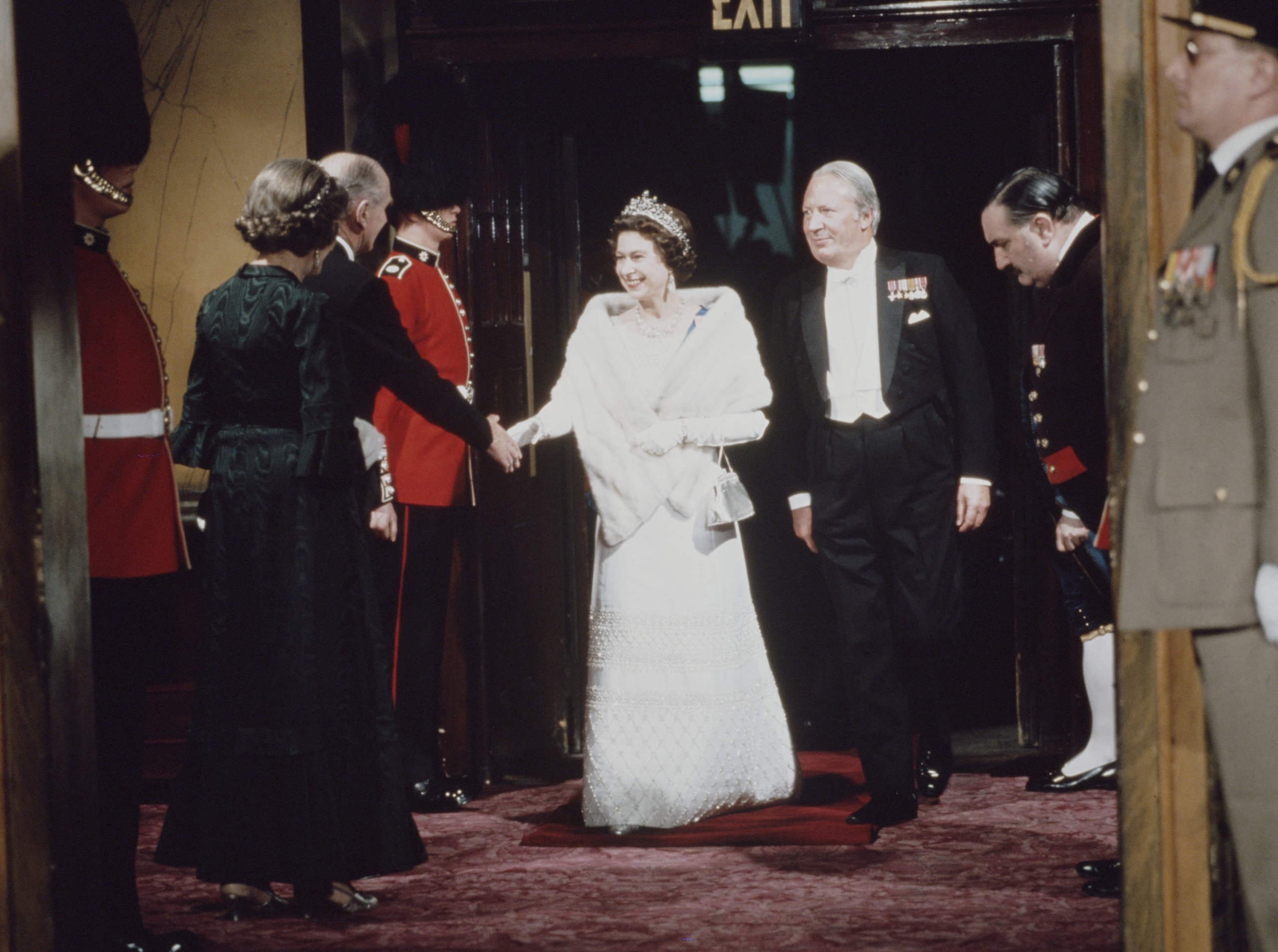 Queen Elizabeth wearing a tiara and white gown shaking hands with someone at a gala
