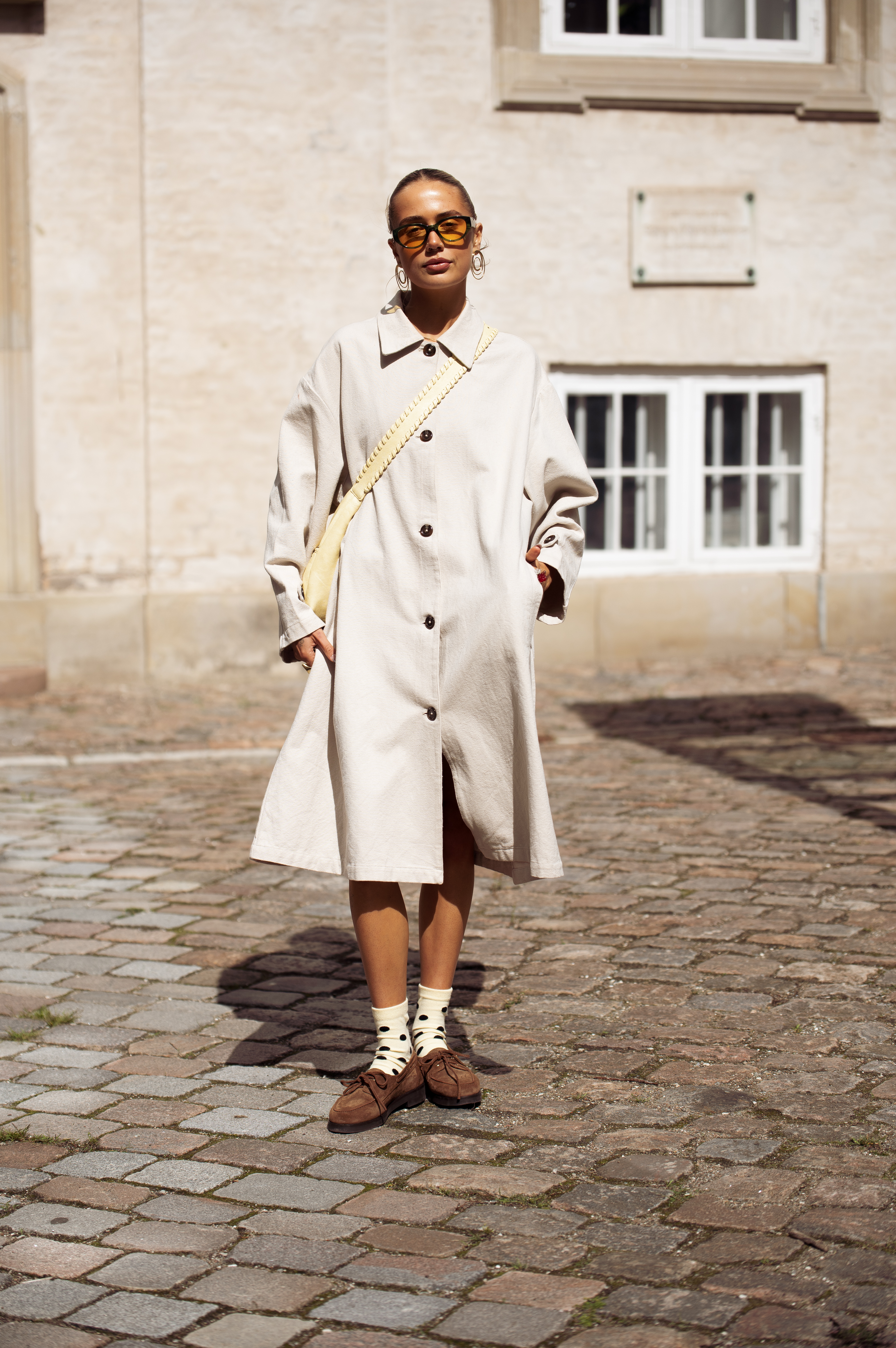 COPENHAGEN, DENMARK - AUGUST 05: A guest wears beige trench coat, yellow socks with black polka dots and brown loafers outside the Skall Studio show during Copenhagen Fashion Week day two on August 05, 2025 in Copenhagen, Denmark. (Photo by Raimonda Kulikauskiene/Getty Images)