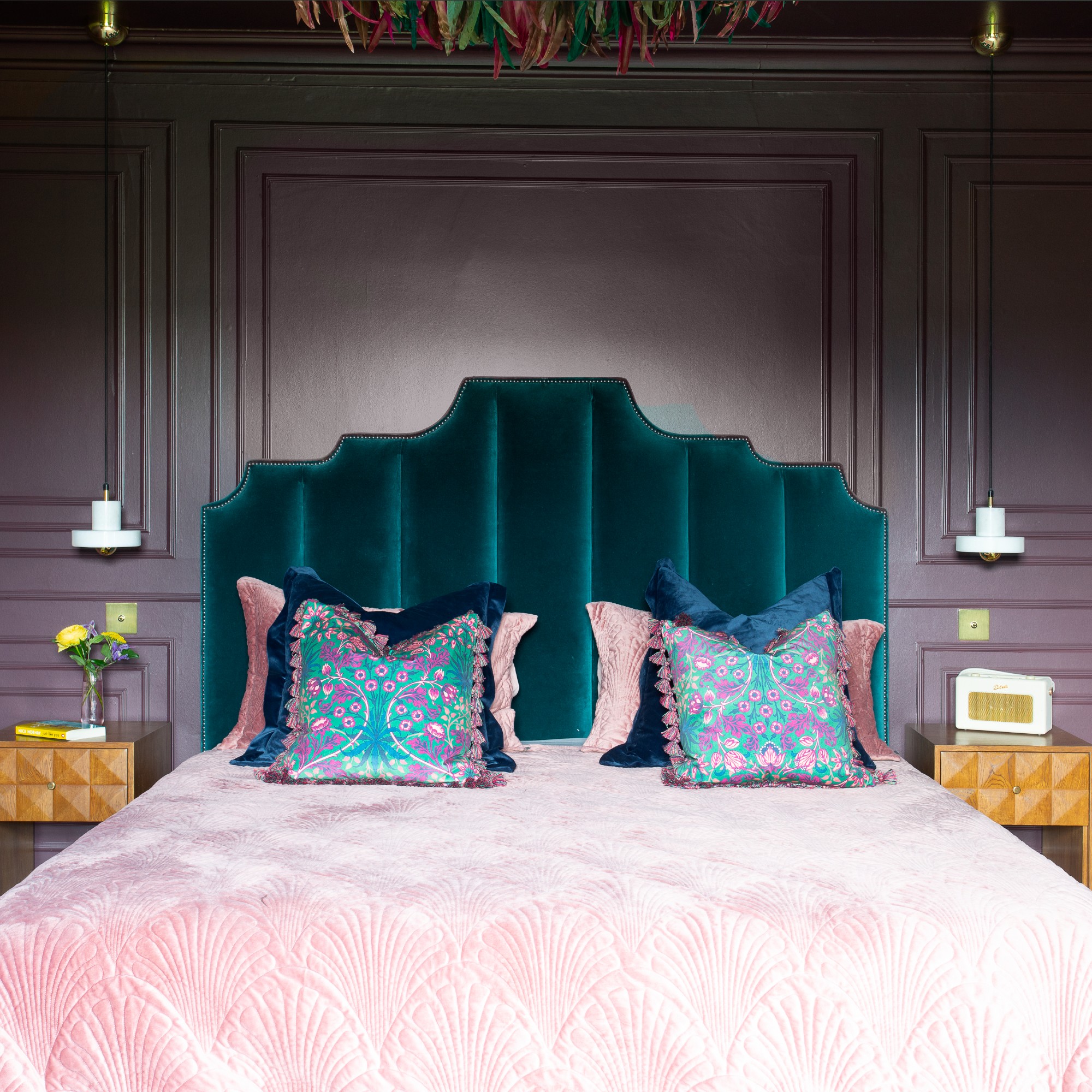 A bedroom painted in aubergine purple with panelled walls and a teal velvet headboard