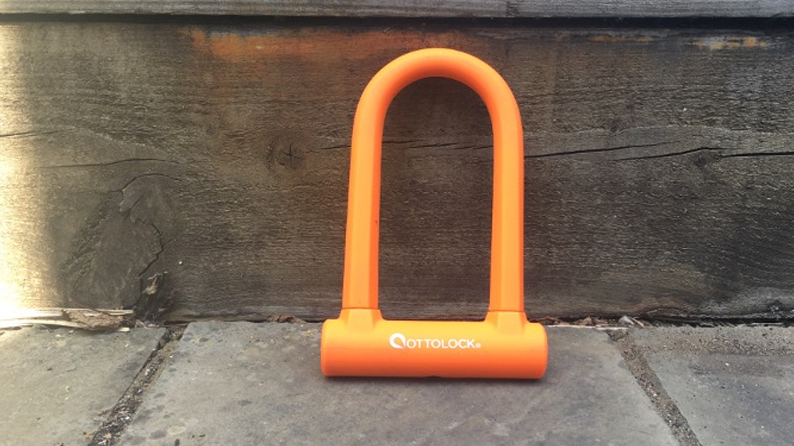 A bright orange Ottolock Sidekick D-lock on paving stones
