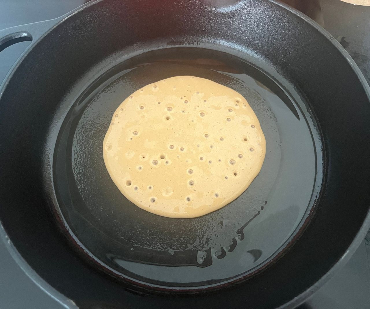Pancake batter bubbling in a black cast iron pan