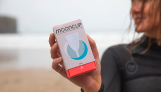 woman on the beach holding a packet containing a Mooncup
