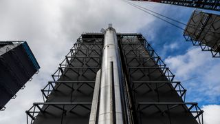 a shiny silver rocket booster stands next to a tall black building.