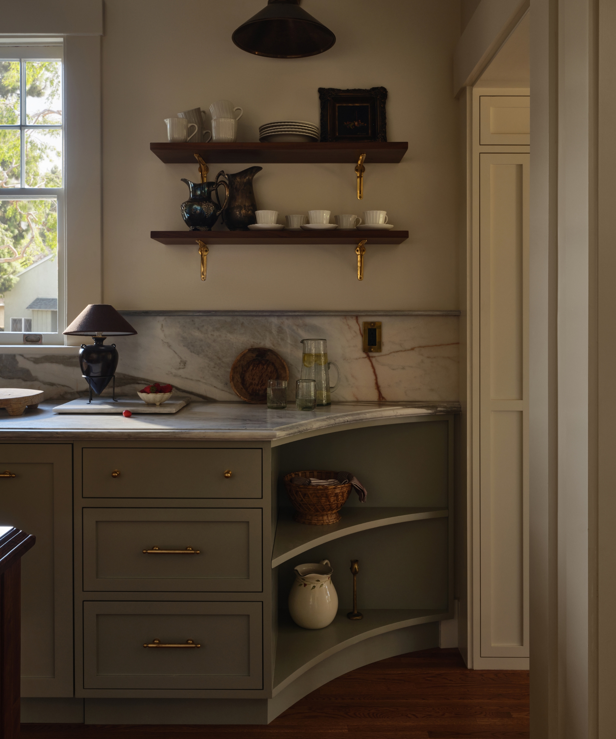 A fall kitchen with soft green cabinet that curve off with open shelving