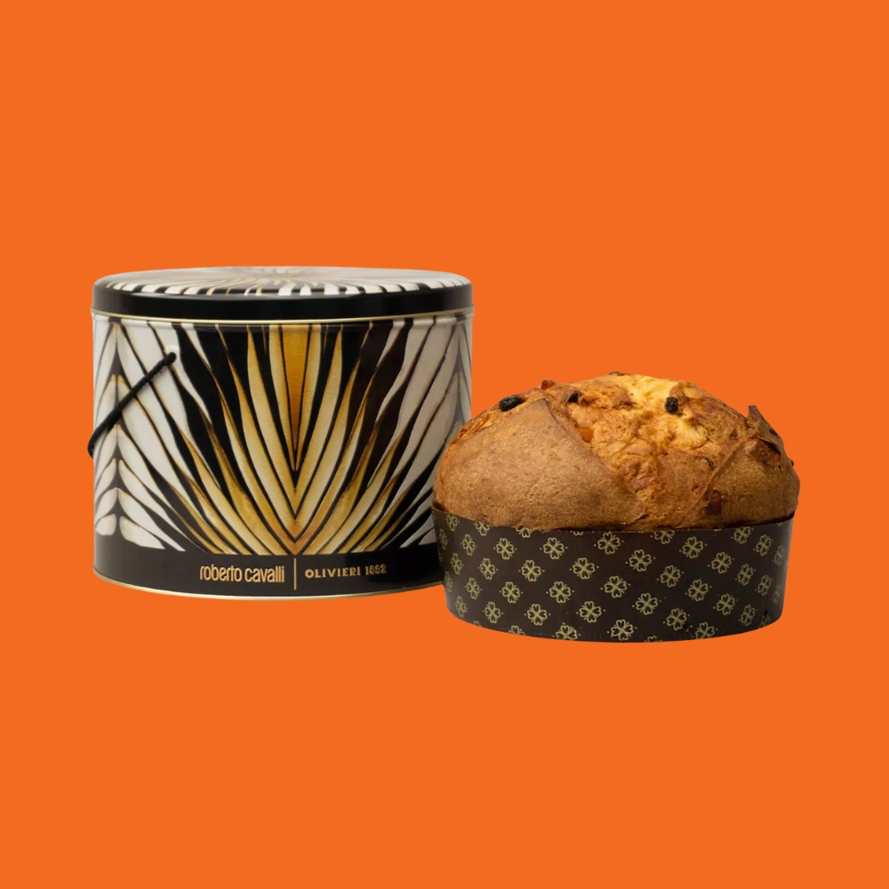 An orange-tinted background on top of which has been placed a print-animalier tin with the logo "Roberto Cavalli | Olivieri 1882" and next to which sits a Panettone.