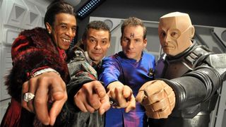 Still from the British sci-fi sitcom called Red Dwarf. Here we see four of the main cast pointing at the camera. From left to right: The Cat, Lister, Rimmer, and Kryten.