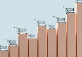 Digital generated image of vertical bar graph made out of golden cubic blocks with shopping carts standing on them against light blue background. Inflation concept.