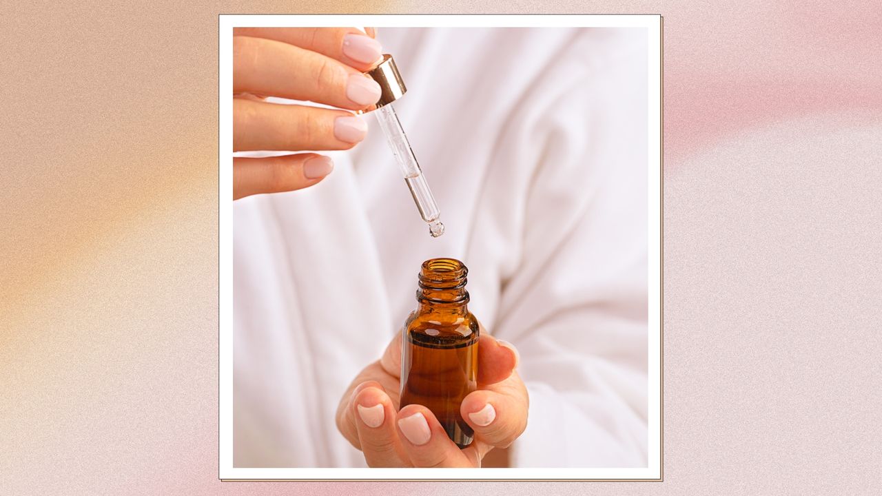 A close up of a woman with a milky pink manicure and wearing a white robe, is pictured holding a brown glass serum bottle/ in an orange and pink gradient template