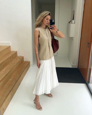 Anouk Yve wearing a tan Liberowe waistcoat, brown suede tote, and white skirt.