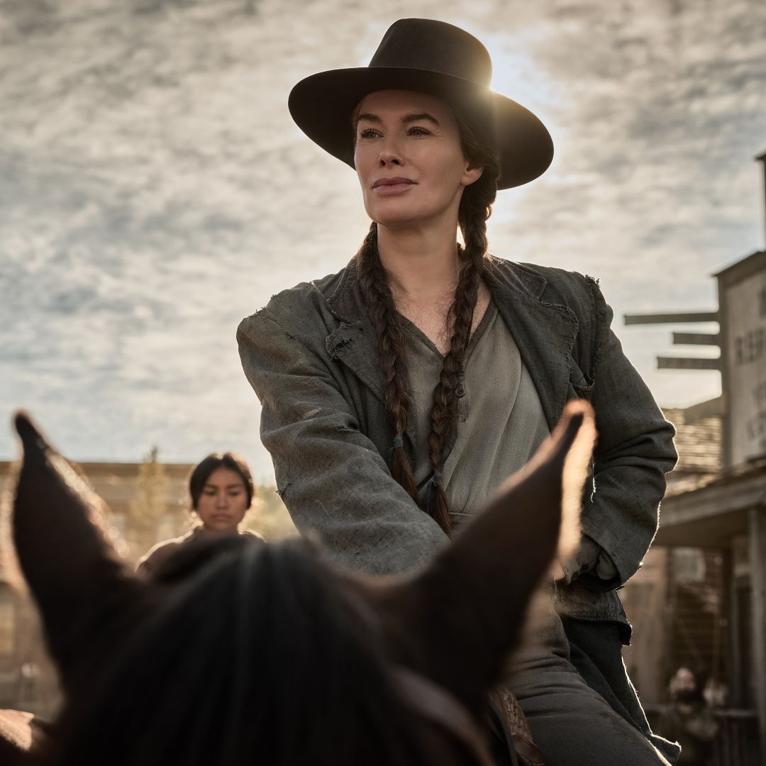 Lena Headey as Fiona Nolan wearing braids and a cowboy hat riding on a horse in a western town square in a still from The Abandons