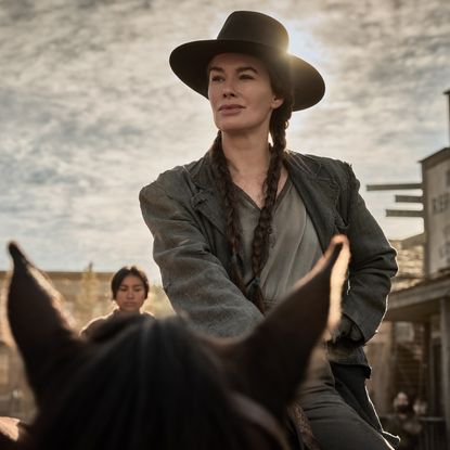 Lena Headey as Fiona Nolan wearing braids and a cowboy hat riding on a horse in a western town square in a still from The Abandons