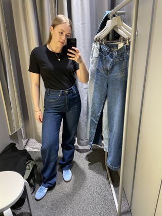 Woman in dressing room wears black t-shirt, blue jeans and blue trainers
