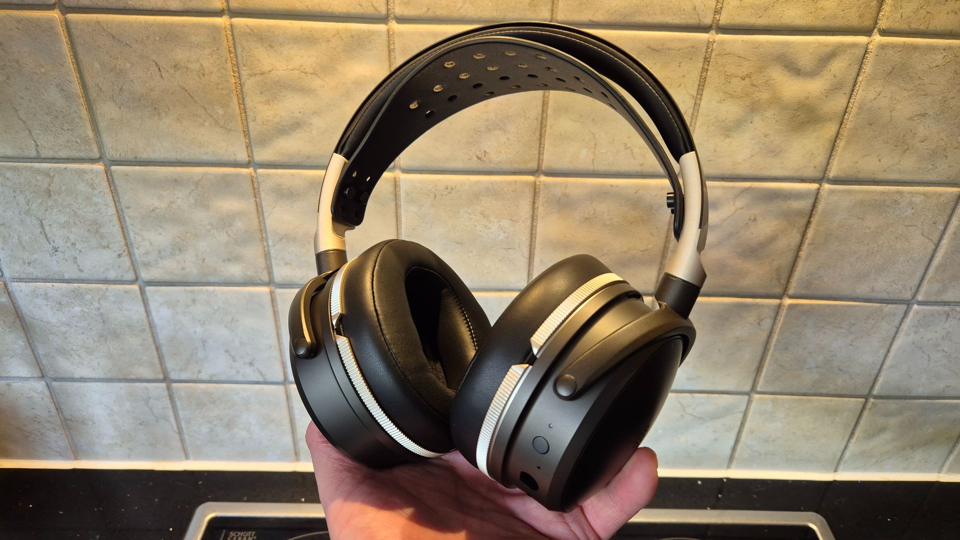 A picture of the Audeze Maxwell 2 ANC gaming headset being held in a hand with pale tiles in the background