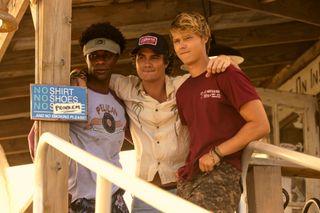 Jonathan Daviss as Pope, Chase Stokes as John B, Rudy Pankow as JJ, standing on the porch of a wooden shack, in episode 401 of Outer Banks.