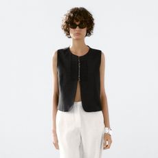 Woman wears black waistcoat and white linen trousers