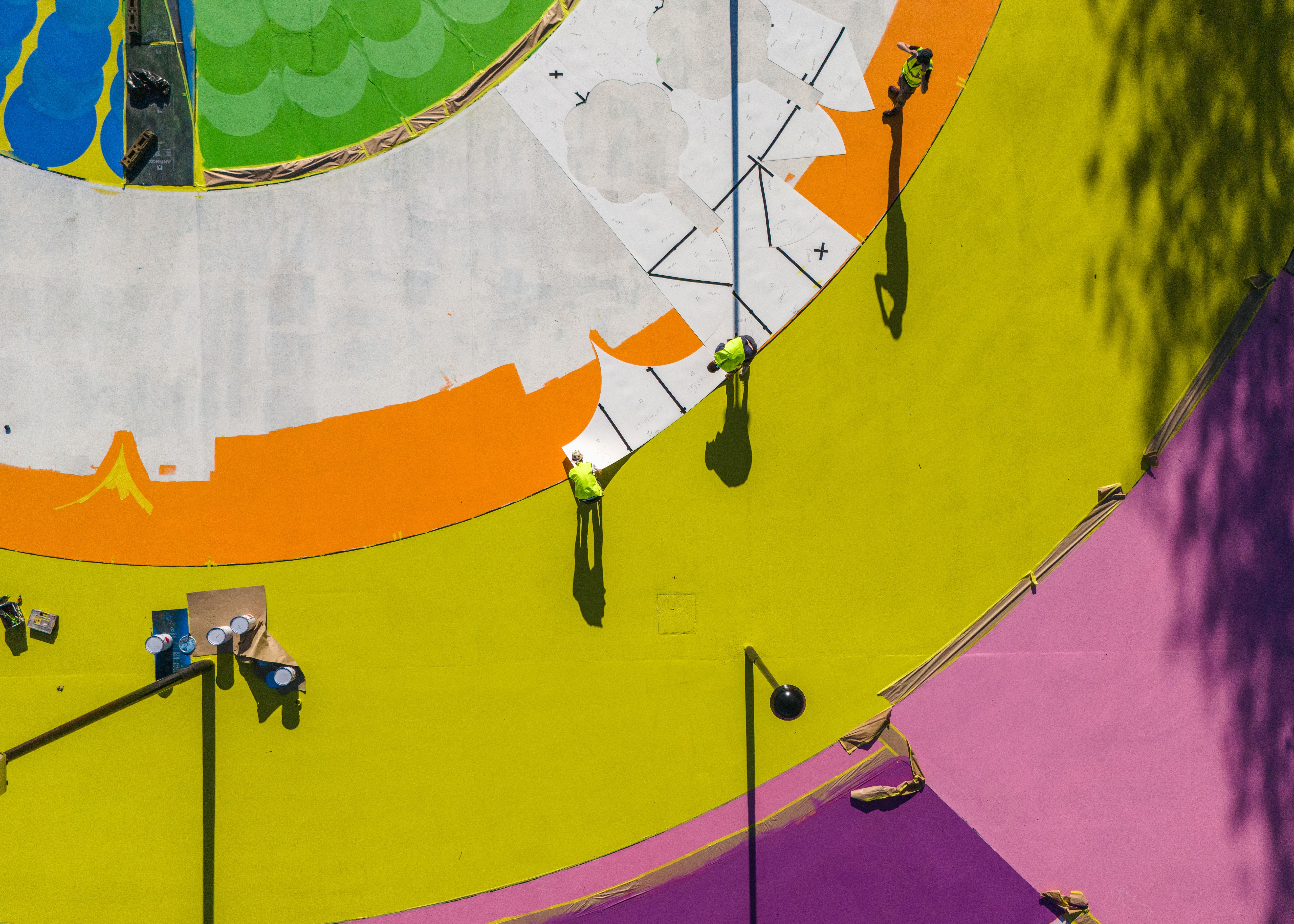 A colorful, concentric mural in yellow, orange, green, and blue, captured in work in progress stages from high above.