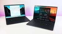 Two dark gray Dell XPS 14 laptops placed side by side on a white desk, one set to light mode and the other displaying a dark mode interface.