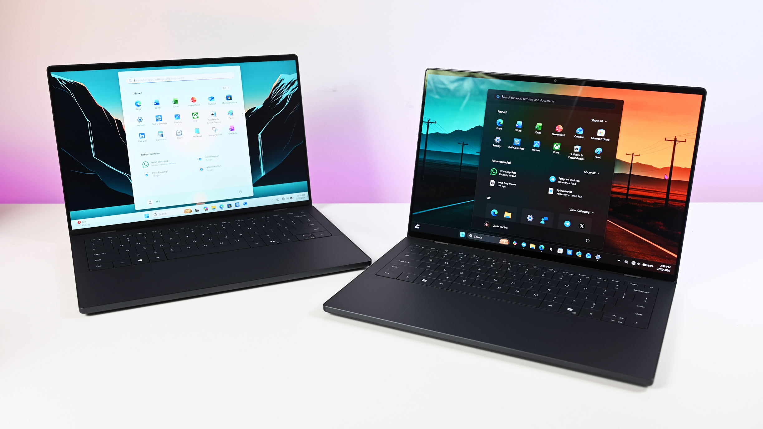 Two dark gray Dell XPS 14 laptops placed side by side on a white desk, one set to light mode and the other displaying a dark mode interface.