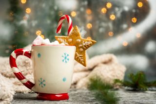 A white mug with blue snowflakes and a candy cane style handle, with a warm, festive beverage on a Christmas decorated surface.