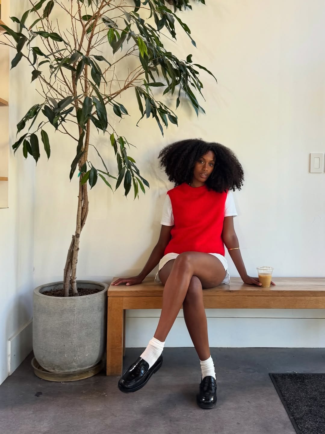 Claire most wearing loafers with a sleeveless red sweater vest over a white T-shirt and shorts.
