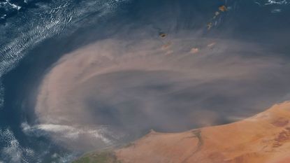 A satellite photo of a large orange dust cloud over the ocean along the coast of West Africa