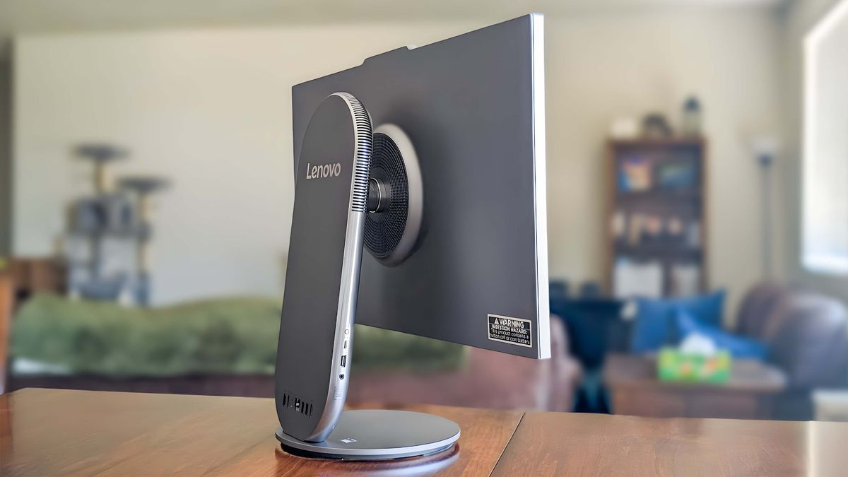 Lenovo Yoga AIO 27" sitting on a table and facing away at an angle so that the back side and the ports on the right side of the stand are visible.