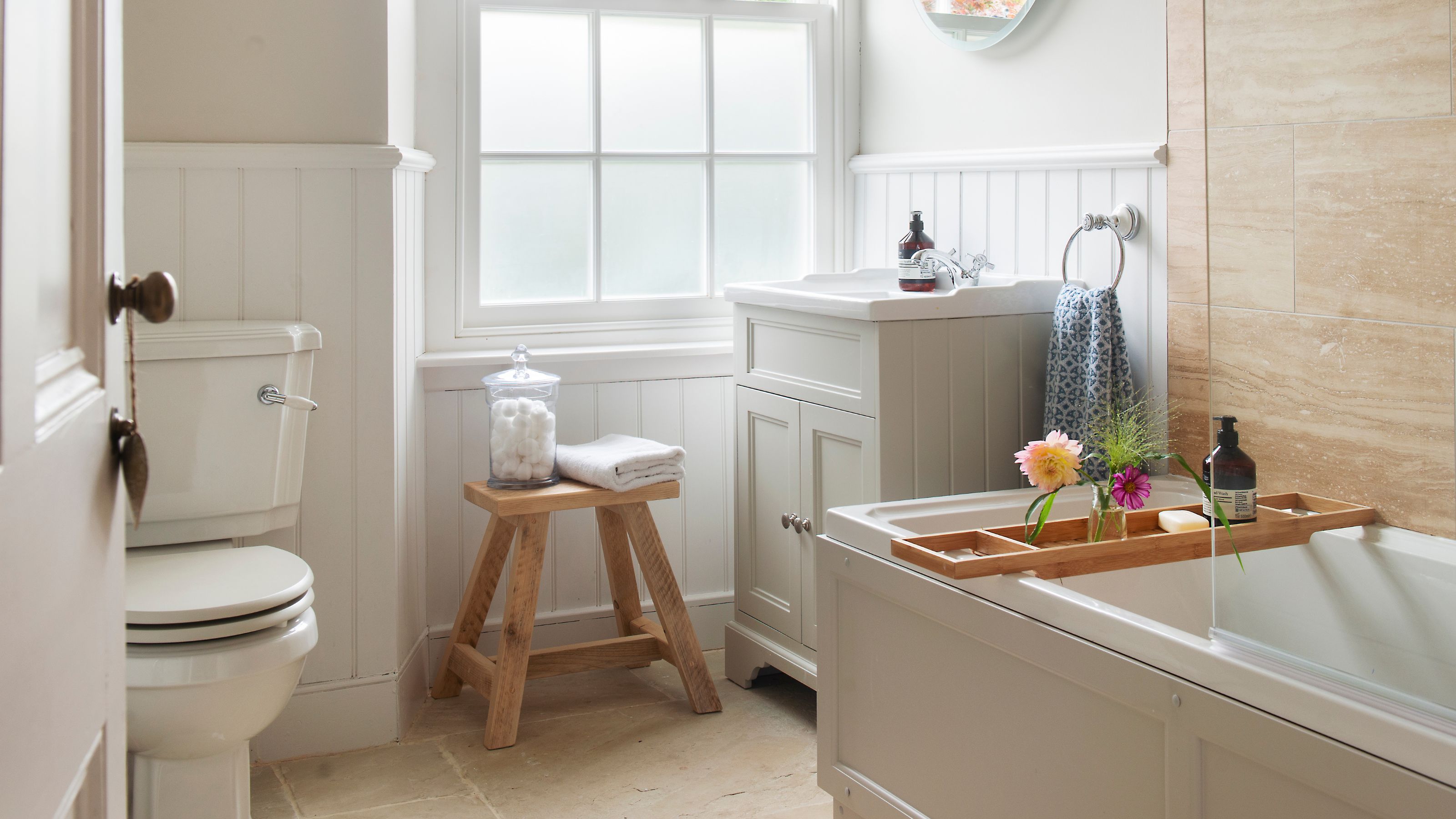 Neutral traditional bathroom, with wall panelling, sash window and wooden stool