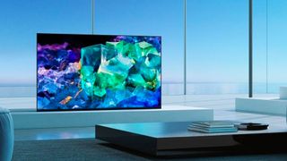 A product shot of the Sony Bravia A95K TV in a bright room with a colourful blue screen