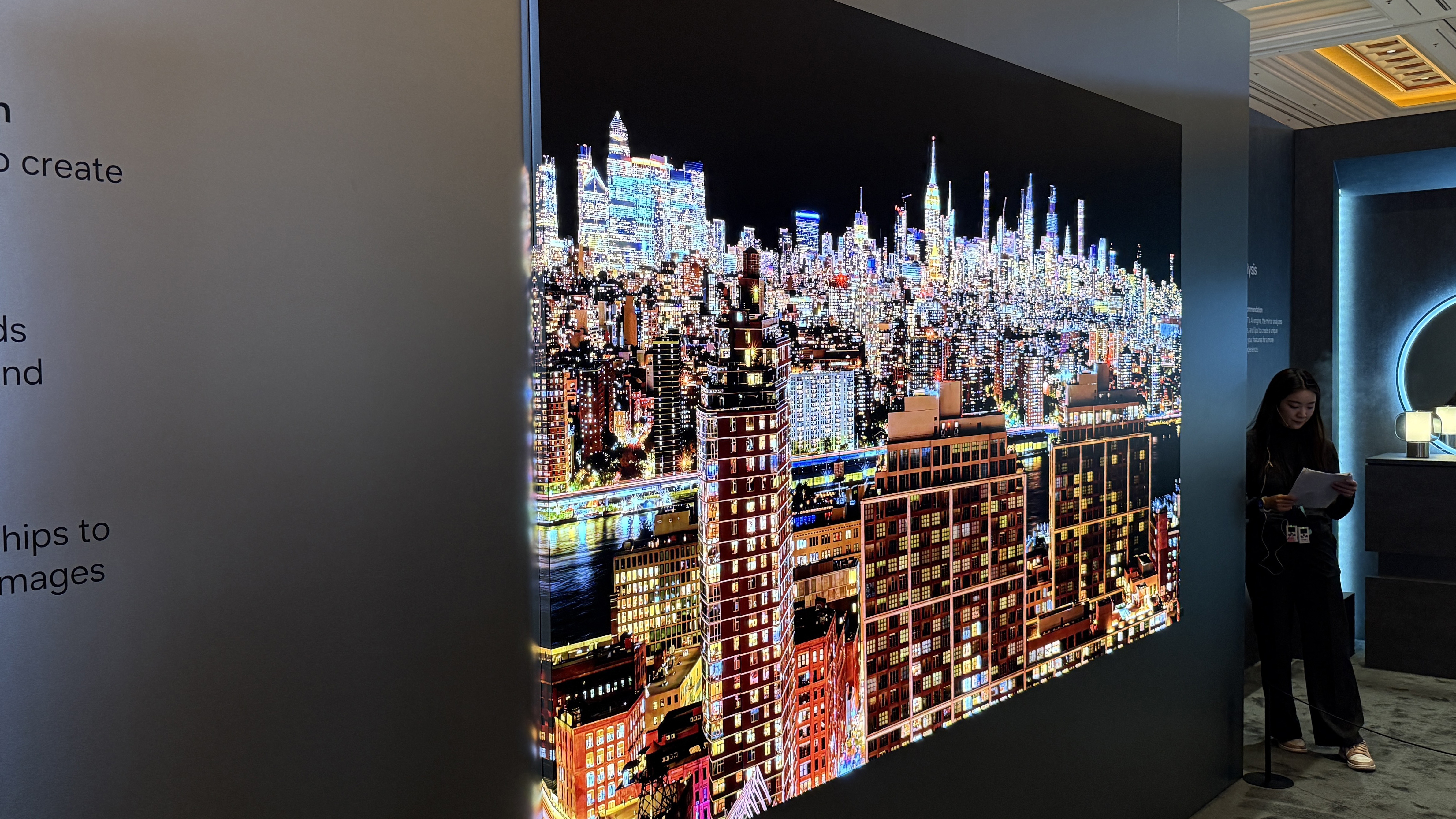 Samsung's 140-inch micro-LED at CES 2026. showing the screen on the side of the TV panel as well as the front TV panel. A night-time image of a city is shown, with brightly lit buildings spilling from the front onto the side screen
