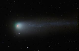 a comet on the right has a red/pink nucleus in the center and a glowing greeny blue coma which stretches out into a long tail to the right.