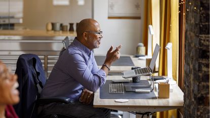 A man sits at his desk while having a video chat on his laptop.