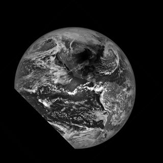 a grey scale image of Earth, with a sliver cut from the left bottom side. A shadow lays near the top.