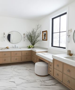 Vanity seating area in neutral bathroom with wooden cabinets and marble counters