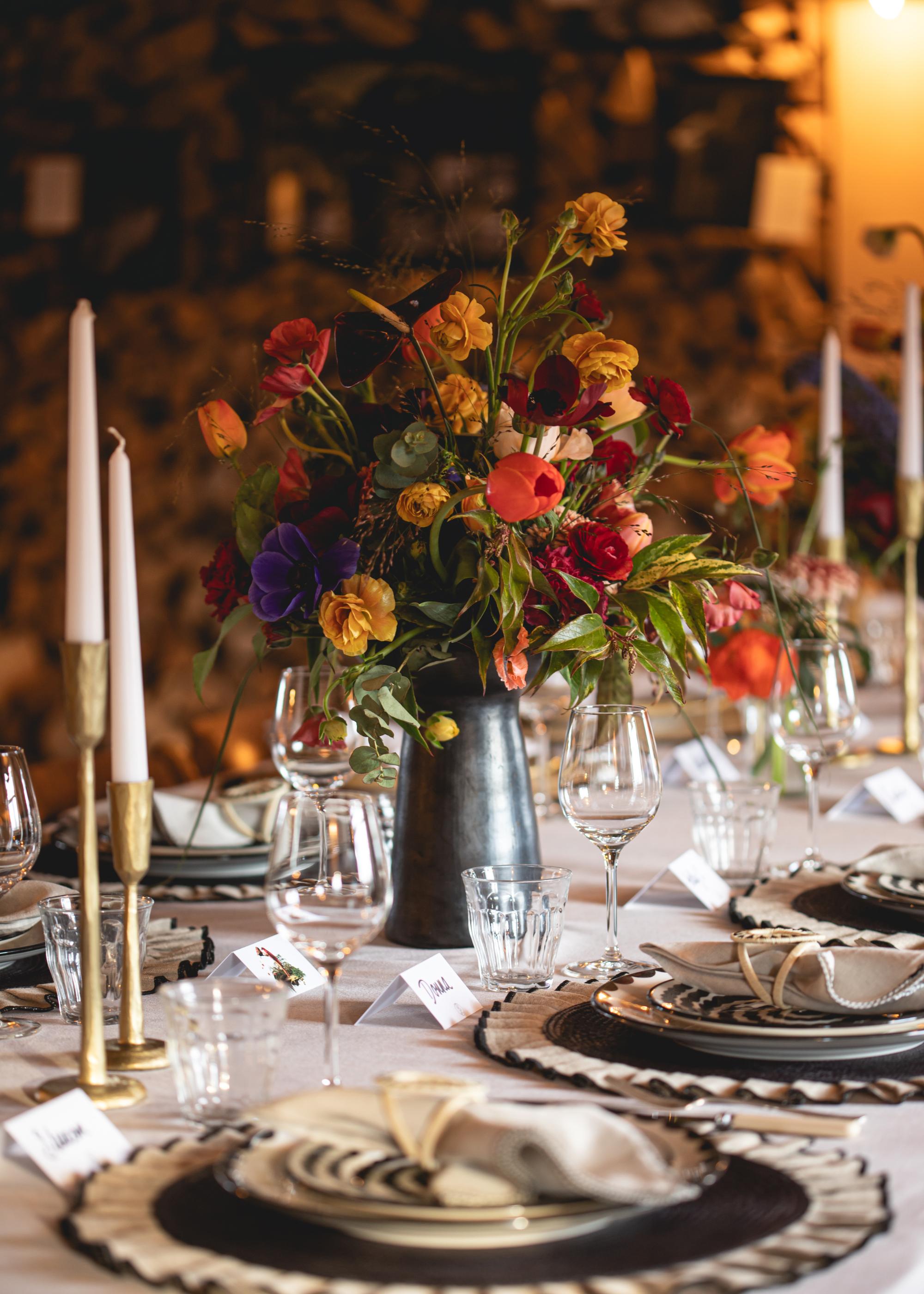 A dining table set with candles, a vase of flowers, namecards, plates and napkins
