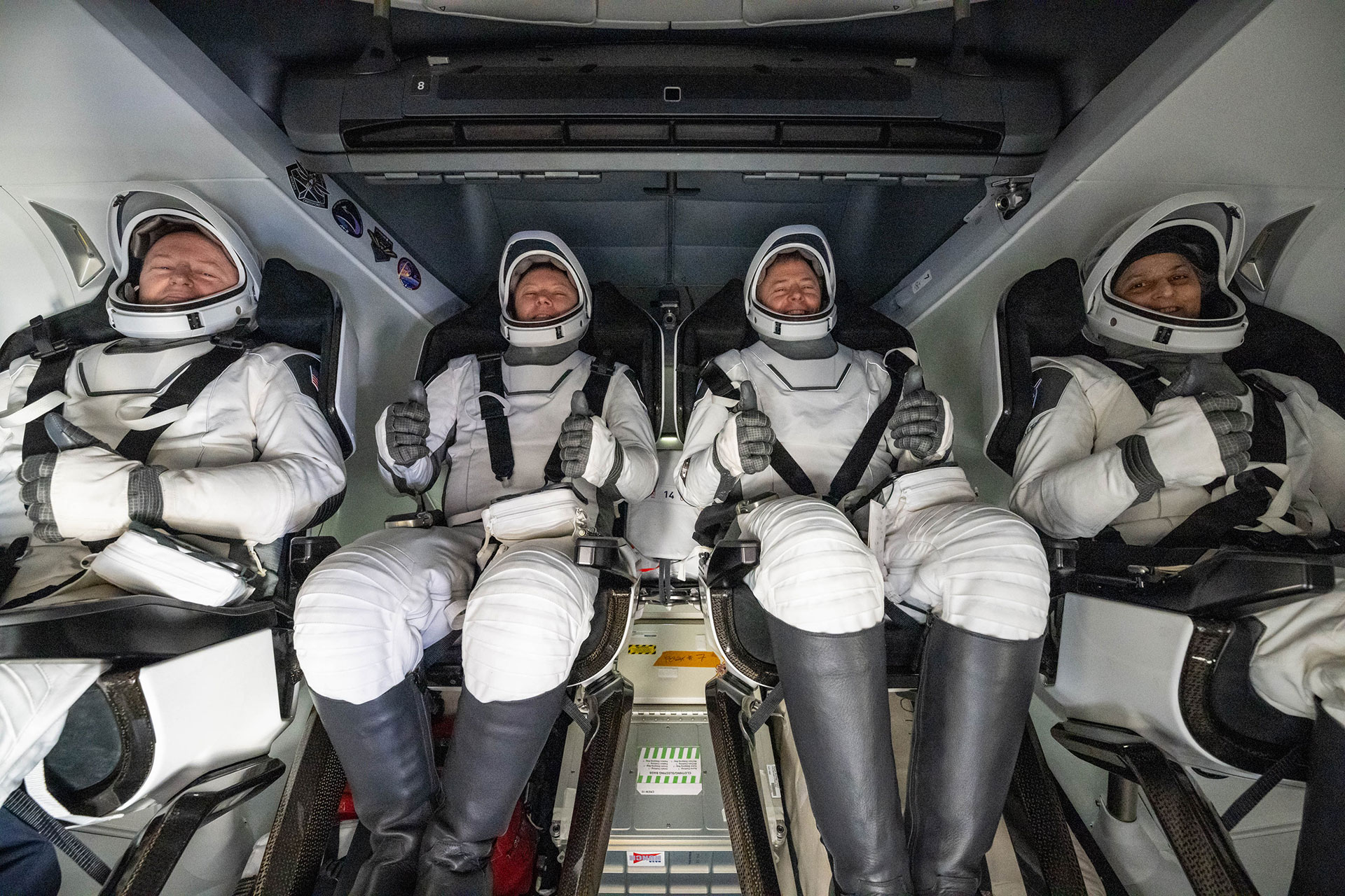 four astronauts in gray and white pressure suits are seen strapped into their seats inside a capsule after splashing down from space