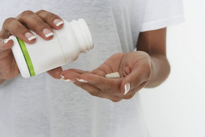 A woman takes a pill from a bottle.