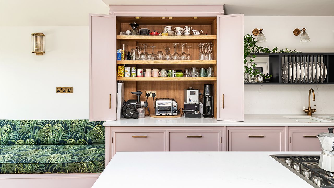 Pink kitchen with shaker cupboards, a green bench and a pantry.