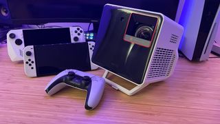 BenQ X300G projector on a wooden desk with Nintendo Switch, Asus ROG Ally, and PS5 controller
