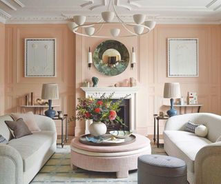 pink living room wiht plaster detail and two sofas and pink upholstered coffee table and white plaster ceiling pendant