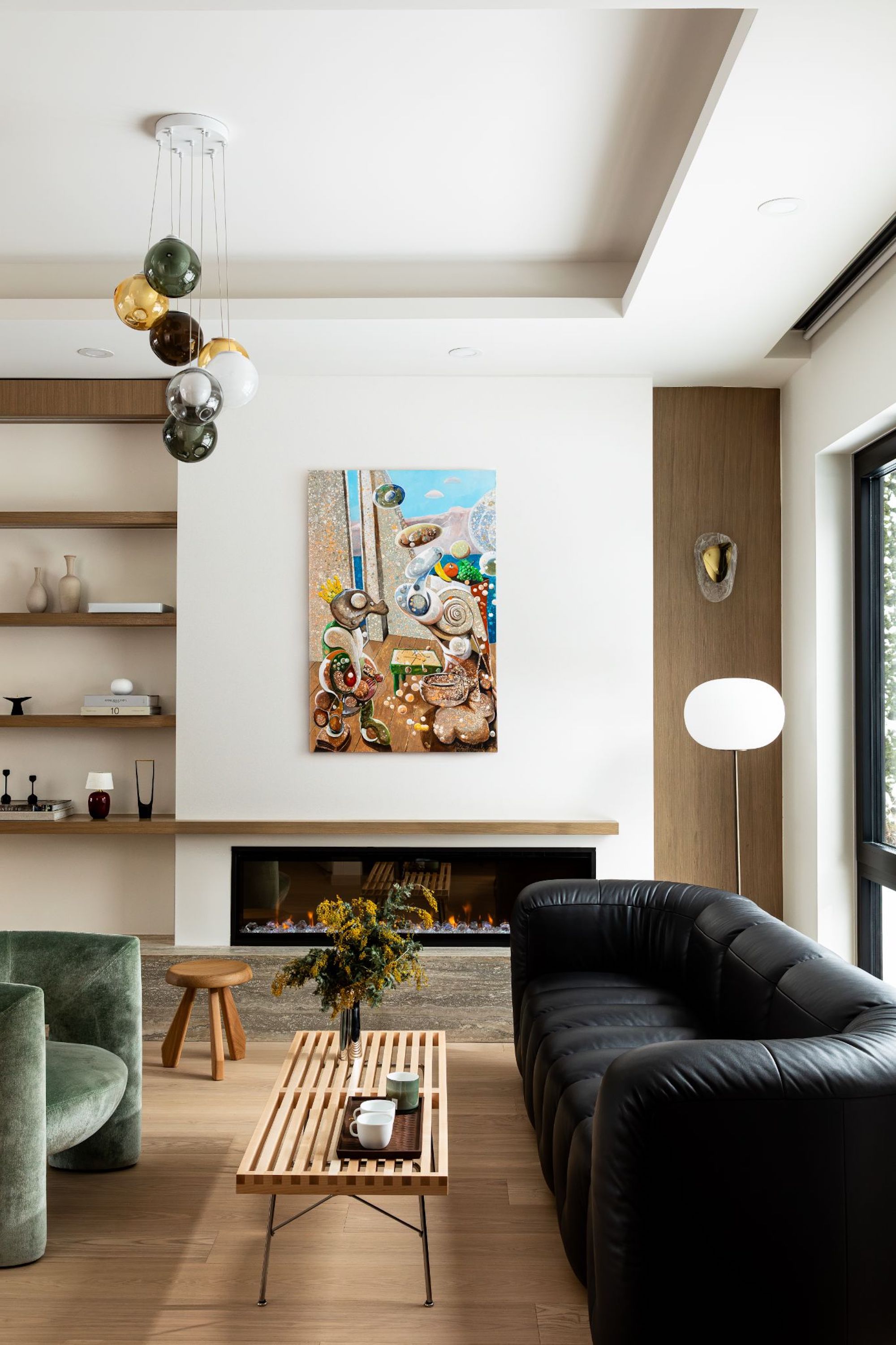 A view of the living space with the modern chandelier above the leather sofa and velvet armchair, with a wooden coffee table in between.