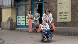 Shelagh and Mrs Wallace stand outside the laundrette watching as Jill walks away pushing Andrew in a wheelchair