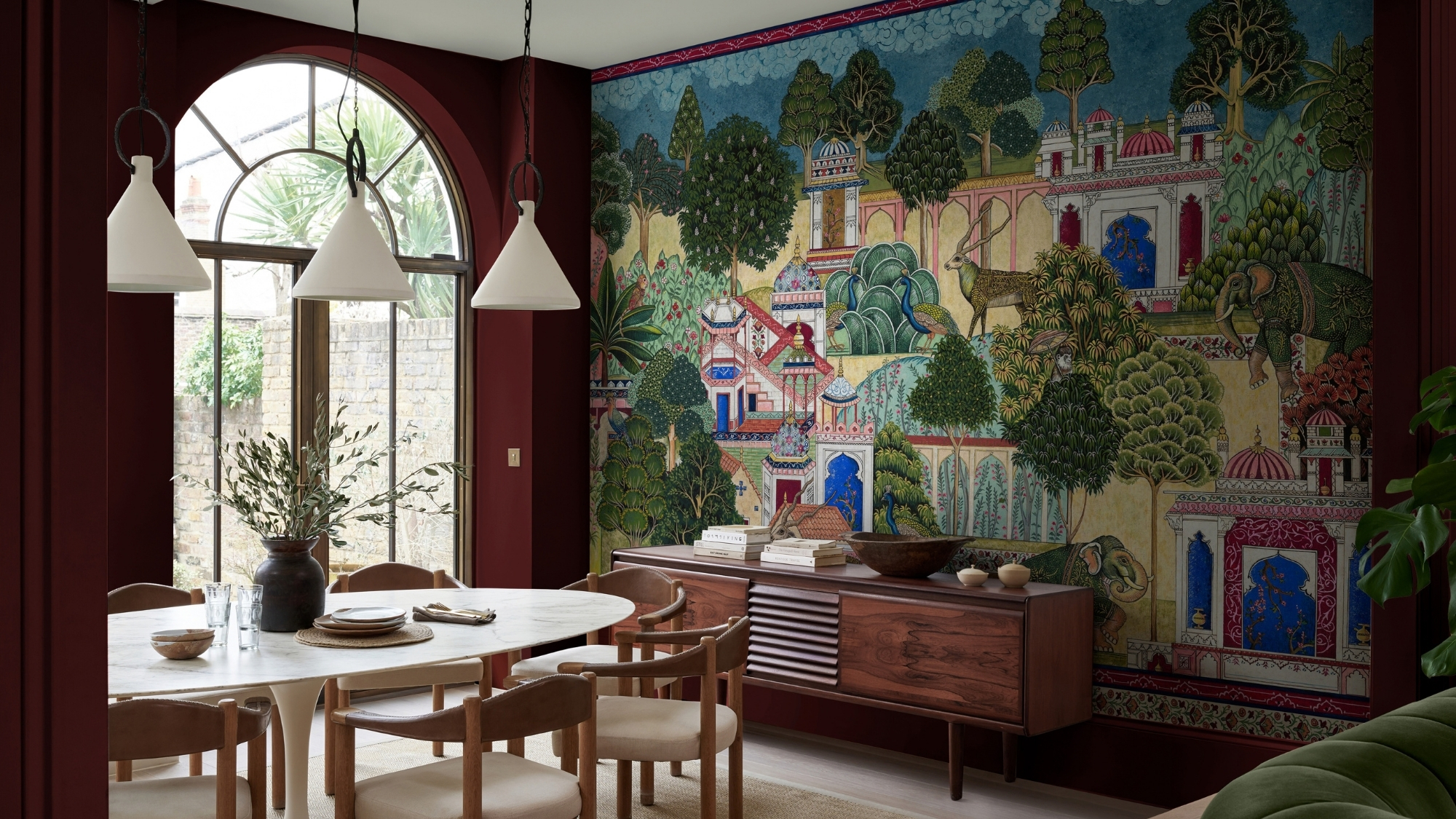 Burgundy dining room with Indian-style mural of palaces, elephants, peacocks; marble table, sideboard, arched window