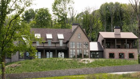 a large dark brick new build home in Tennessee with sloped grass front lawn and surrounded by trees