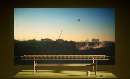 A steel mesh bench shown in front of a photograph showing a sky at sunset and a city skyline