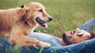 Man lying on his back on grass with his dog resting on his stomach