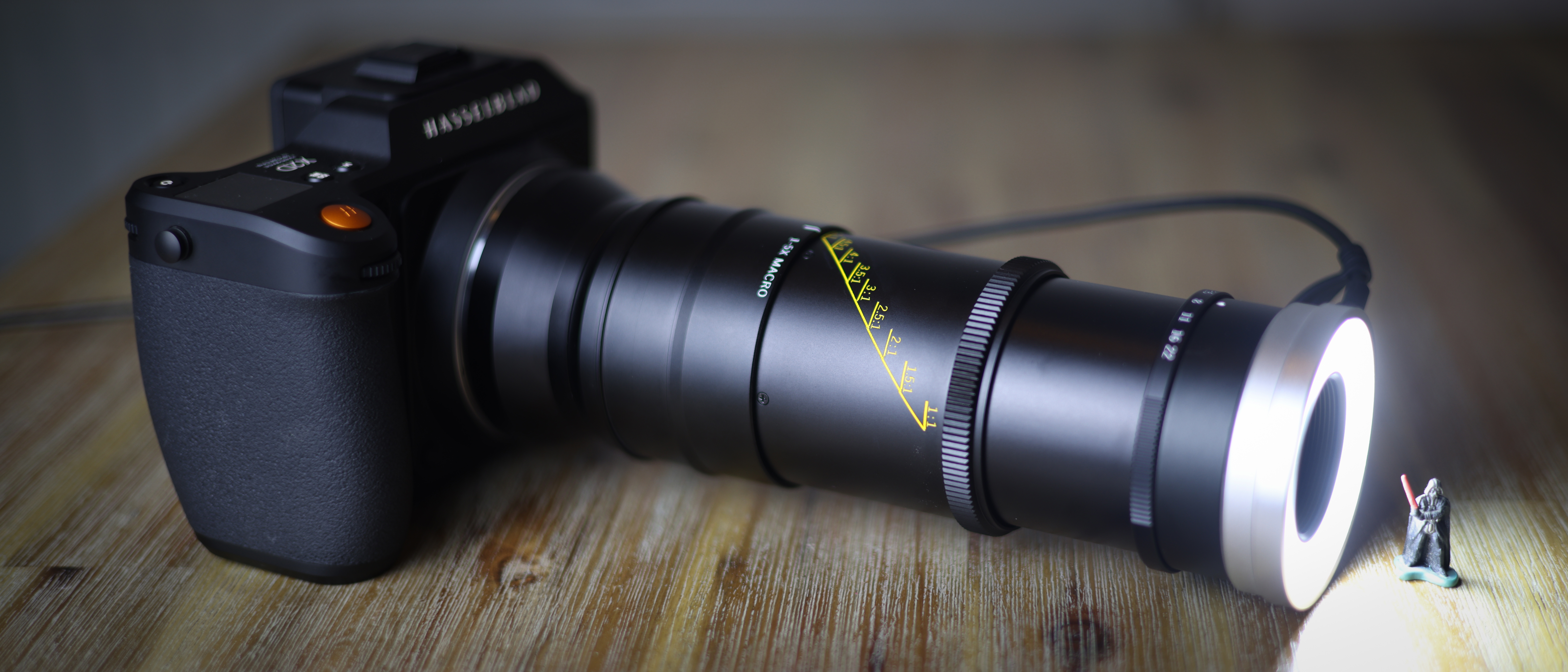 Mitakon 55mm f/2.8 1-5x Macro on a wooden surface, with the lighting attachment